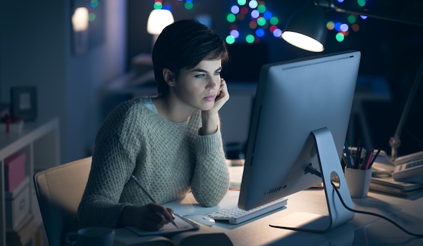 Kvinna sitter framför en dator på kvällen och tittar fokuserat på skärmen