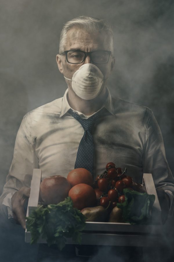 Man med munskydd i förorenad miljö håller i grönsaker